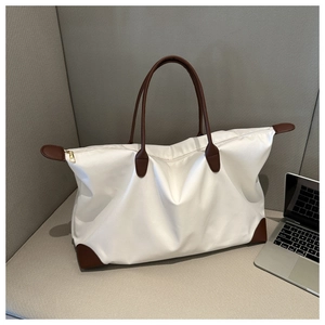 Detalle de un gran bolso de viaje de nailon blanco con asas de cuero marrón y cremallera