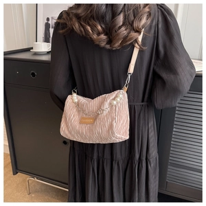 Detail of pink pleated crossbody bag with pearl chain and fashion patch on black dress