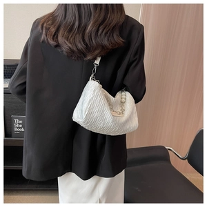 Detail of white pleated satin shoulder bag with pearl and metal chain strap on model