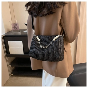 Detail of black pleated shoulder bag with white pearl and silver chain strap on a model