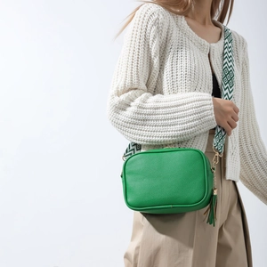 Fashionable green camera bag with wide geometric strap and fringe detail on white outfit