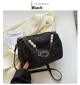 Detail of pleated black crossbody bag featuring pearl strap accents and fashion tag