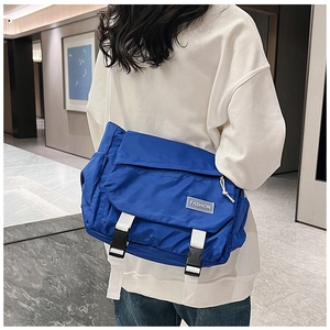 Detail of blue nylon messenger bag featuring white straps and durable buckle closures