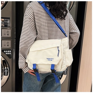 Detail of cream messenger bag featuring blue straps and brand patch in laundry room