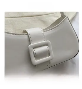 Close-up of the large buckle detail and fine stitching on the white leather baguette bag