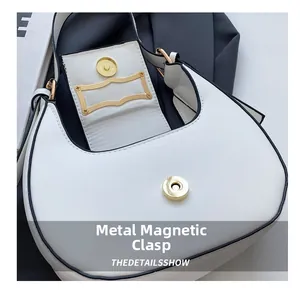 Detail view of the white crescent bag showing golden magnetic buckle closure and oil edge