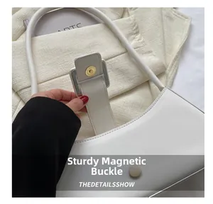 Detail shot of the secure gold magnetic clasp on a white faux leather baguette bag