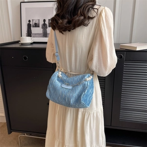 Sky blue pleated nylon crossbody bag with pearl chain handle on an ivory dress model