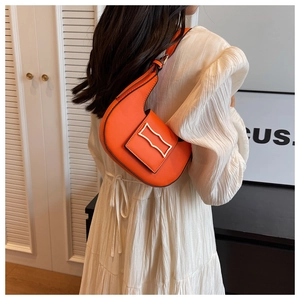 Close-up of vibrant orange crescent shoulder bag with metallic clasp on white dress
