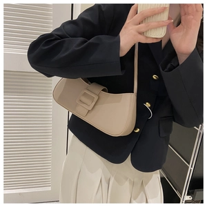 Gros plan du sac baguette minimaliste beige avec grande boucle carrée porté à l'épaule