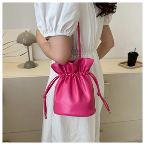 Detail of rose pink drawstring bucket bag shown with white dress in minimalist interior