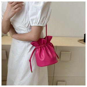 Detail of rose red drawstring bucket bag with soft leather pleats worn by a model