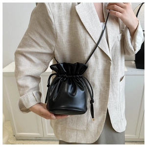 Close-up of black leather bucket bag with gold-tone drawstring details on model