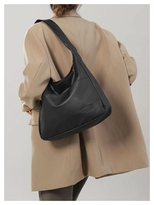 Detail view of a large black leather tote bag featuring a minimalist rectangular patch