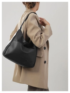 Side view of a large black minimalist hobo shoulder bag worn with a khaki trench coat