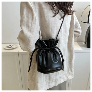 Detail of black faux leather bucket bag with drawstring closure and slim shoulder strap
