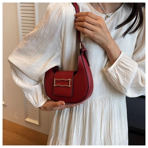 Detailed view of a red crescent hobo bag with a gold buckle on a white pleated dress