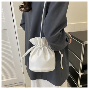 Modern white drawstring bucket bag shown from a side view on a model in gray blazer