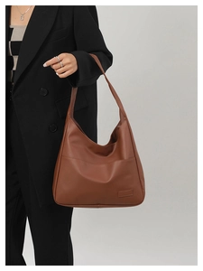 Brown faux leather tote bag shown on a black suit model in a minimalist studio setting