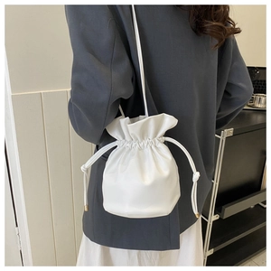 Close-up of white drawstring bucket bag with gold metal hardware and slim shoulder strap