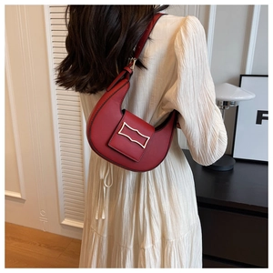 Detail of red crescent shoulder bag with gold metal buckle on white pleated dress