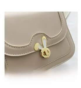 Close-up of beige leather crossbody bag featuring a golden rabbit-shaped twist lock