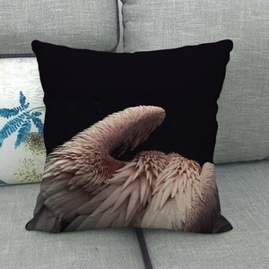 Detail of pink feather print on black square pillowcase placed on a gray fabric sofa