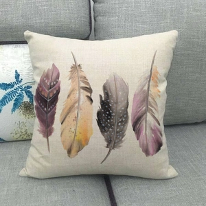 Detail of square linen pillowcase featuring artistic watercolor feather prints on sofa