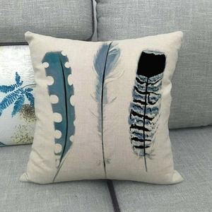 Close-up of linen pillow cover featuring blue bird feather patterns on a grey fabric sofa