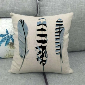 Detail of square linen pillowcase featuring three artistic feather prints on grey sofa