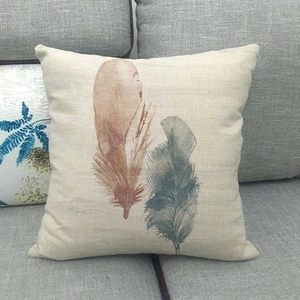 Close-up of linen pillowcase featuring two watercolor feathers on a grey sofa