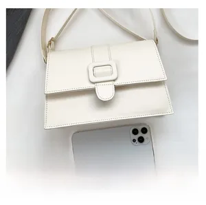 Minimalist white square crossbody bag size comparison with a smartphone on desk
