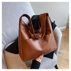Close-up of brown soft leather tote bag featuring a front pocket on a grey chair