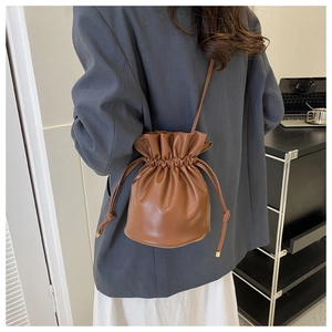 Detail view of brown leather bucket bag with drawstring closure and gold metal tips