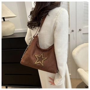 Brown suede hobo bag with star patch and chain strap detail on model in home setting