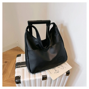 Close-up of black tote bag featuring a front pocket, placed on a white suitcase for travel