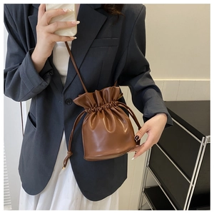 Brown drawstring bucket bag styled on model with grey suit and white dress