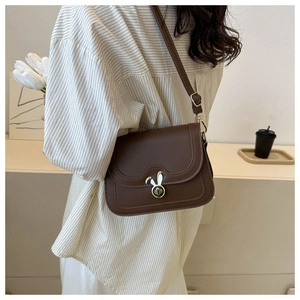 Detail of brown crossbody bag featuring a golden rabbit-ear rotating lock and matte leather