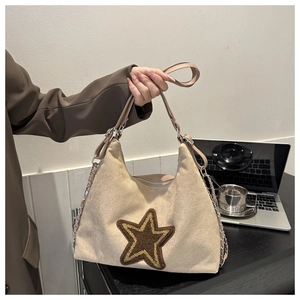 Detail of beige tote bag featuring a brown plush star patch and chain shoulder strap