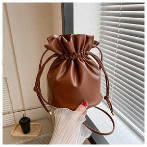 Detail of a brown leather drawstring bucket bag with soft texture and slim shoulder strap