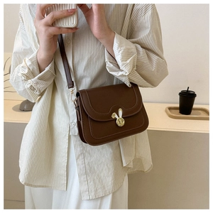 Detail of a brown leather shoulder bag featuring a gold rabbit-ear lock and wave-cut flap