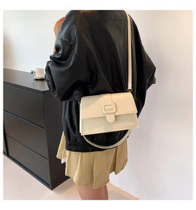 Side view of a beige minimalist small square bag with textured buckle on a model
