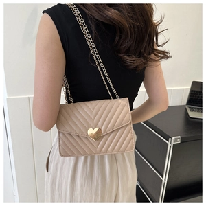 Sac bandoulière beige avec matelassage en V et fermoir cœur doré porté par un modèle