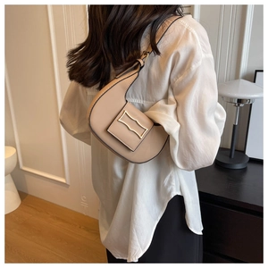 Close-up of a beige crescent moon bag featuring a gold rectangular metal buckle detail