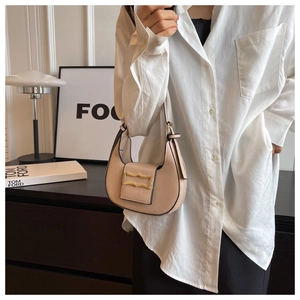 Chic beige crescent shoulder bag with wavy gold buckle shown on a model in a white shirt