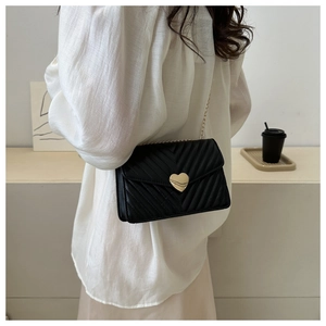 Détail du sac bandoulière noir avec texture matelassée en V et fermoir cœur doré
