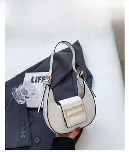 Detail of creamy white crescent bag with elegant wavy gold metal buckle and PU leather texture