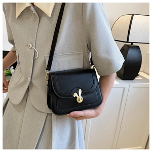 Detail view of a black leather crossbody bag featuring a golden rabbit-shaped metal clasp