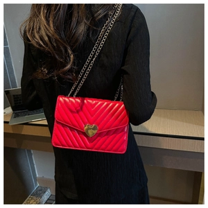 Détail d'un sac matelassé rouge avec fermoir coeur doré et bandoulière en chaîne