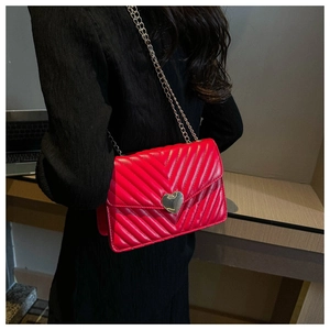 Détail du sac rouge matelassé en V avec boucle cœur dorée et bandoulière chaîne en métal
